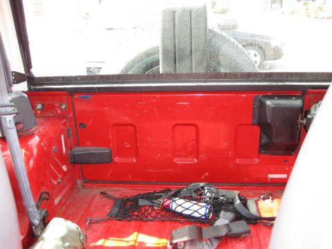 1998 Jeep Wrangler - The interior of a red Jeep cargo area shows a spare tire and a cargo net, with another vehicle visible outside.