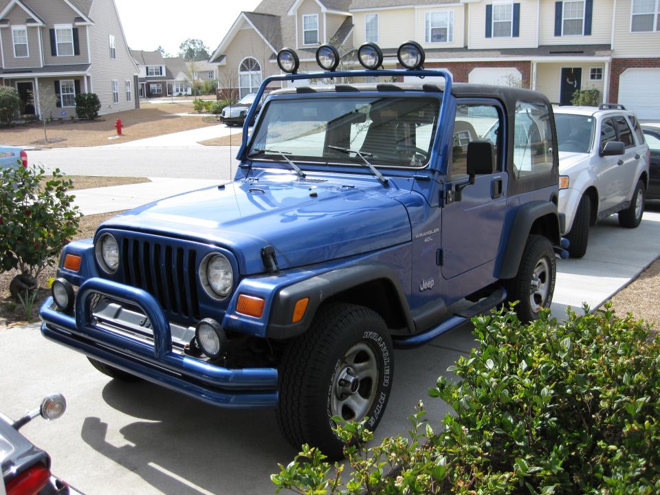 Blue Jeep Wrangler TJ with light bar on roof, parked in driveway next to a silver SUV