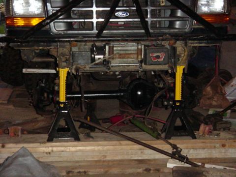1992 Ford Bronco - The front end of a 1992 Ford Bronco is elevated on jack stands for maintenance, revealing its undercarriage and winch system.
