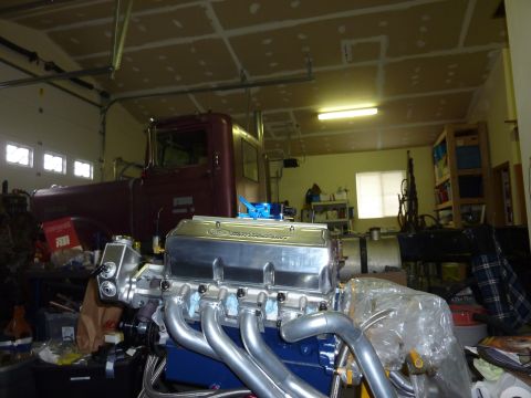 1971 Ford Mustang - A V8 engine with Ford Motorsport valve covers sits in front of a maroon truck in a garage.