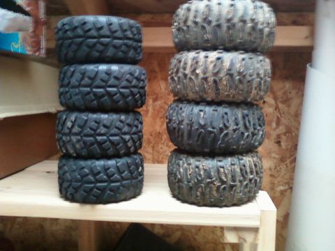 1996 Ford Bronco - Two stacks of four off-road tires are displayed on a wooden shelf in a storage area.