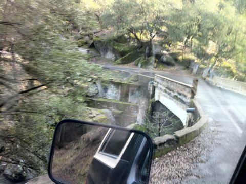 1989 Ford Bronco - A view from inside a vehicle shows a road and a small bridge over a ravine, with a reflection of the vehicle in the side mirror.