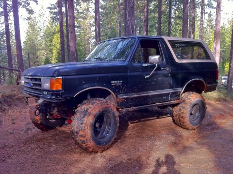 1989 Ford Bronco - This 1989 Ford Bronco is equipped with large off-road tires and appears to be on a dirt trail in a wooded area.