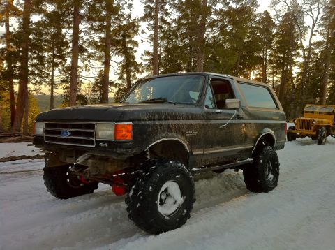 1989 Ford Bronco - A lifted 1989 Ford Bronco sits in the snow, with a yellow Jeep visible in the background.