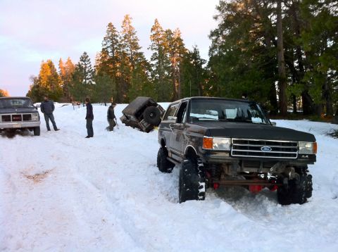 1989 Ford Bronco - Multiple vehicles stuck in snow, including an overturned SUV and a modified Ford Bronco.