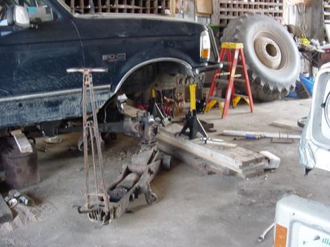 1992 Ford Bronco - The vehicle is undergoing mechanical work in a cluttered garage setting with a large tire visible in the background.