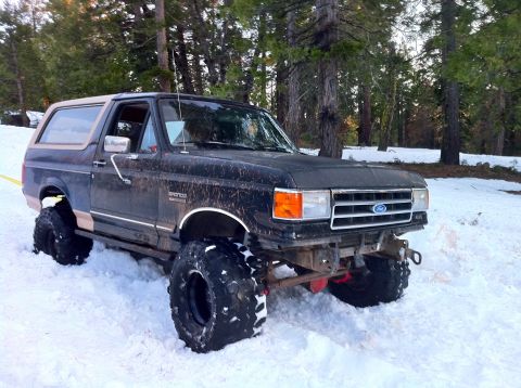 1989 Ford Bronco - This lifted Ford Bronco is parked in the snow with large off-road tires. The front end is equipped with a winch.