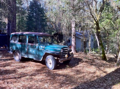 1989 Ford Bronco - Old green station wagon sits in a wooded area next to a small cabin.