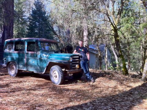 1989 Ford Bronco - A man poses with a weathered Jeep Willys Station Wagon parked in a wooded area next to a small cabin.
