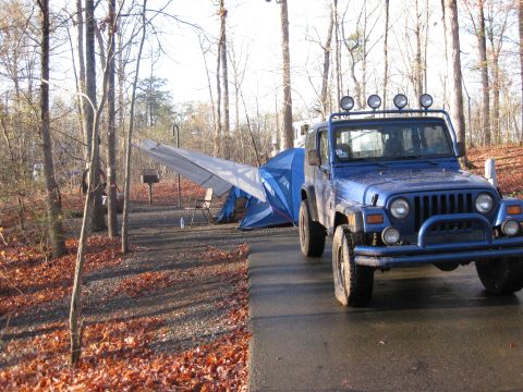 1998 Jeep Wrangler - A blue 1998 Jeep Wrangler is parked at a campsite next to a blue tent and camping equipment.