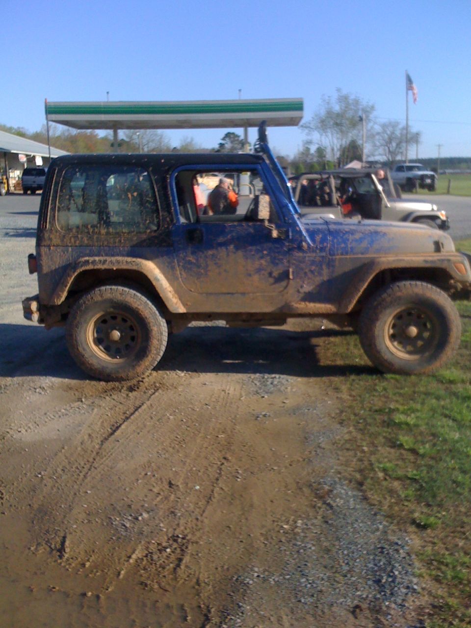 Mud-covered blue Jeep Wrangler, side view. Appears to be a 1997 model
