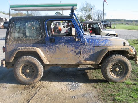 1998 Jeep Wrangler - A muddy blue Jeep Wrangler is parked at a gas station with another Jeep visible behind it.
