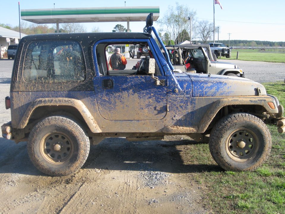 Mud-splattered blue Jeep Wrangler parked next to another Jeep at a gas station