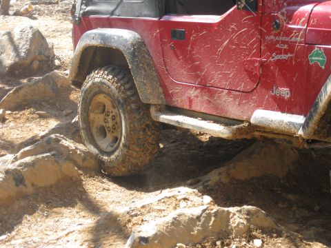 1998 Jeep Wrangler - A red 1998 Jeep Wrangler 4.0 Sport navigates a rocky, off-road trail.
