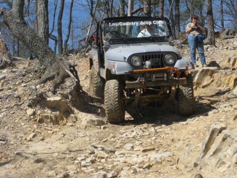 1998 Jeep Wrangler - Jeep Wrangler navigates a challenging off-road trail with rocky terrain and trees.