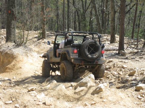1998 Jeep Wrangler - This Jeep Wrangler is navigating a challenging, rocky path through a wooded area.