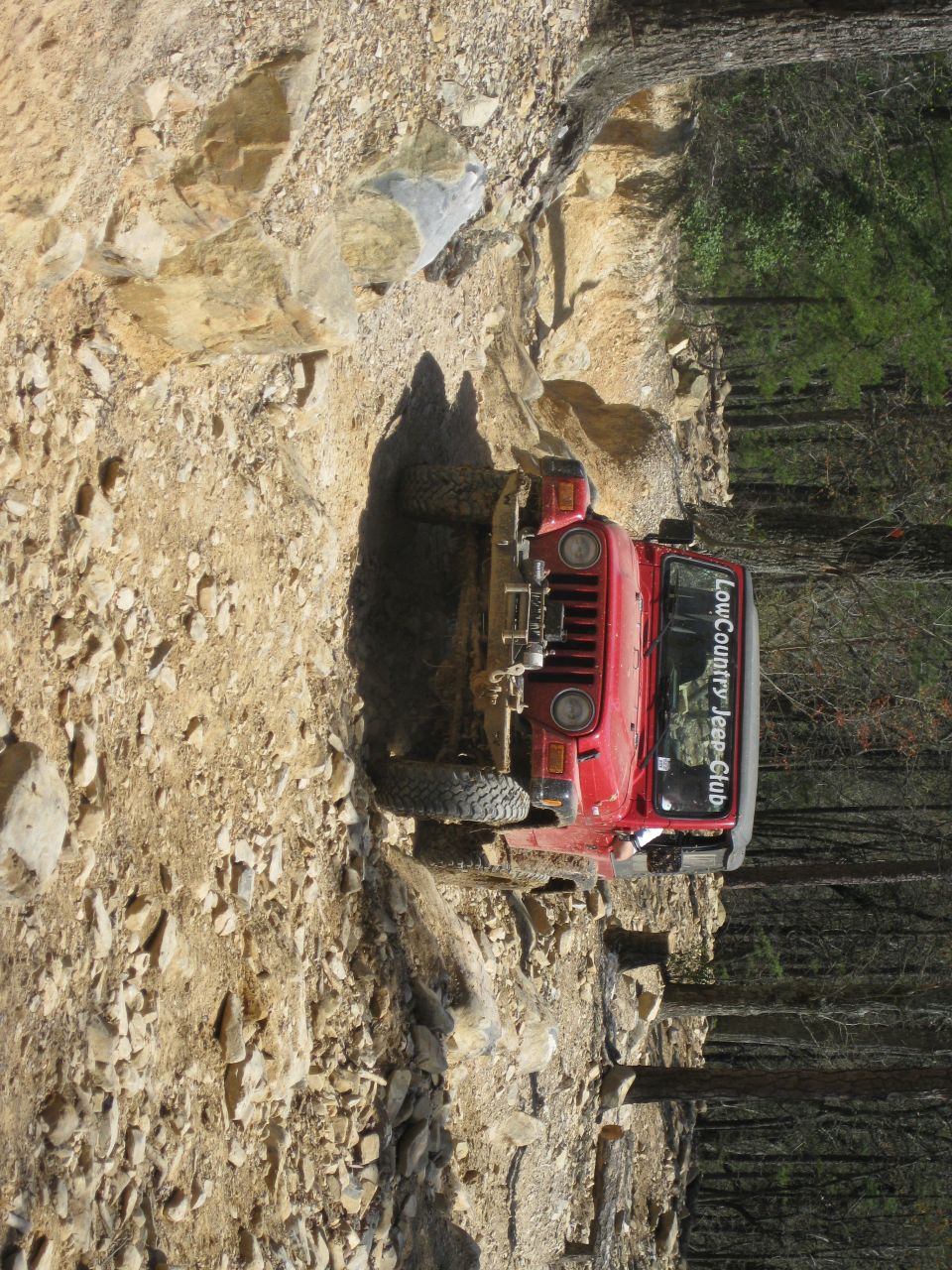 Red Jeep Wrangler navigating a rocky incline with trees in the background