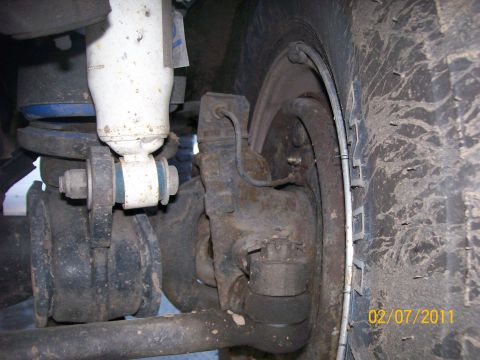 1970 Ford Bronco - Close-up view of the front suspension and tire of a vehicle, showing rust and wear.