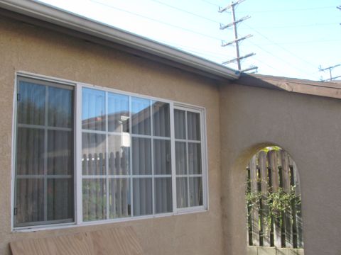 1968 Ford Mustang - Exterior of a tan stucco house showing a large white-framed sliding window with grid muntins, an arched stucco opening onto a wood fence at…