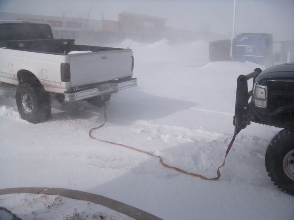 Two trucks connected by a tow strap in a snowy environment