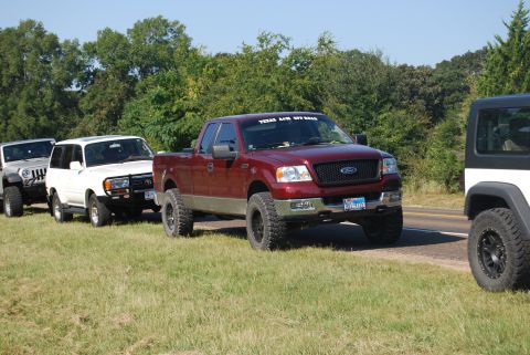2005 Ford F-150 - A line of off-road vehicles, including a maroon Ford F-150, are parked on the side of a road.