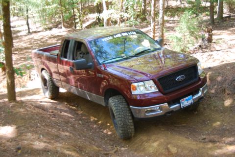 2005 Ford F-150 - Maroon Ford F-150 truck driving on a dirt trail surrounded by trees.