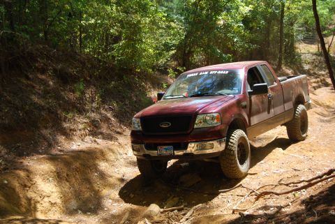 2005 Ford F-150 - A lifted Ford F-150 navigates a muddy trail surrounded by trees.