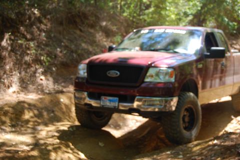 2005 Ford F-150 - Maroon Ford F-150 truck navigates a dirt path in a wooded area.