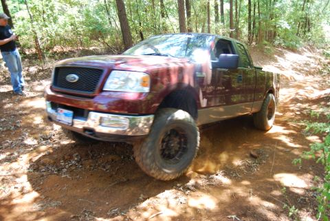 2005 Ford F-150 - A maroon Ford F-150 navigates a wooded trail with its front tire raised.