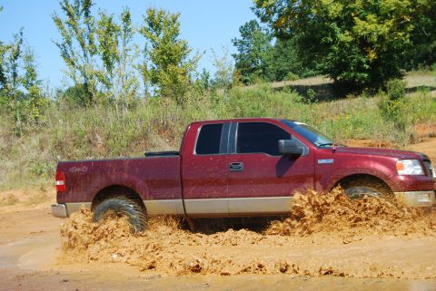 2005 Ford F-150 - Red 2005 Ford F-150 navigating a muddy trail, kicking up a large spray.