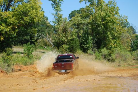 2005 Ford F-150 - A red Ford F-150 truck splashes through a muddy track surrounded by trees.