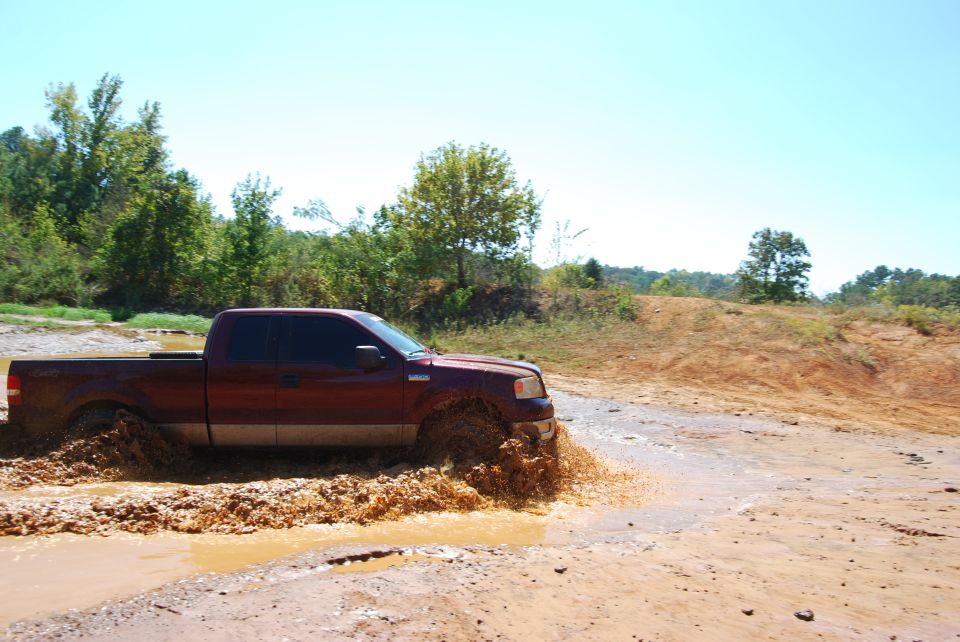 Red Ford F-150 splashing through a muddy track