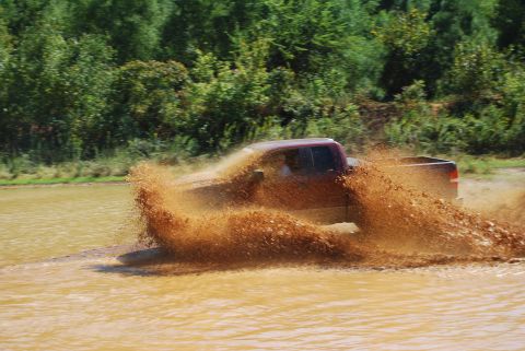 2005 Ford F-150 - Truck splashing through mud, with trees in the background.