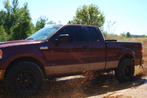 2005 Ford F-150 - A maroon pickup truck splashes through a muddy puddle on a sunny day.