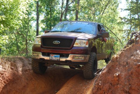 2005 Ford F-150 - A maroon Ford F-150 navigates a challenging off-road trail, with a Texas A&M Off-Road sticker visible on the windshield.