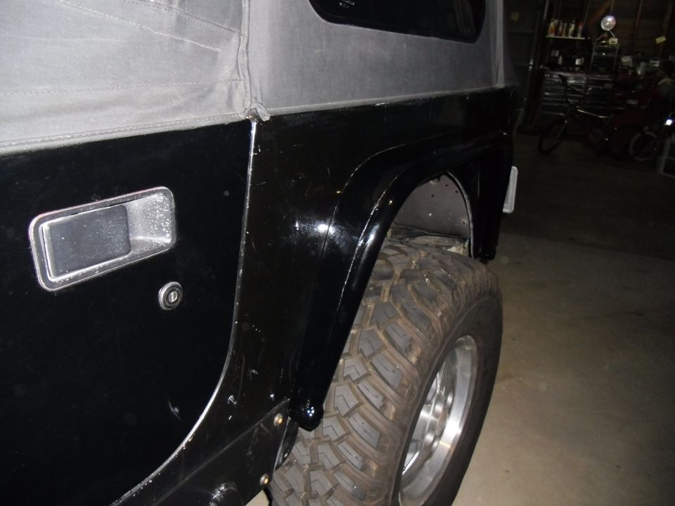 Black Jeep Wrangler, rear fender and tire, side view, showing minor scratches on the body