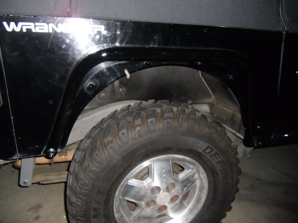 Close-up of a black Jeep Wrangler's rear fender and tire. The word WRANGLER is visible on the fender