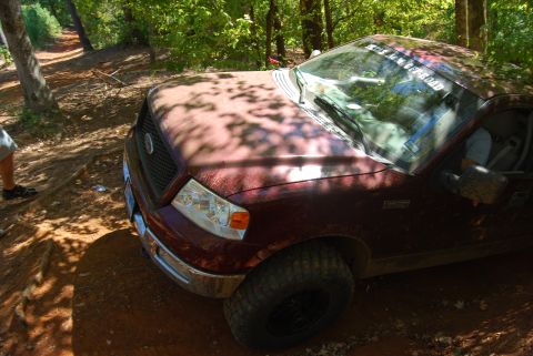 2005 Ford F-150 - A maroon Ford F-150 navigates a muddy off-road trail surrounded by trees.