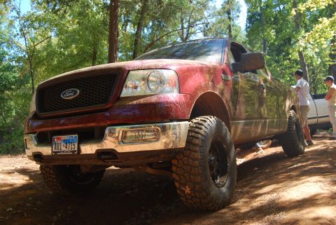 2005 Ford F-150 - This red Ford F-150 is shown off-road with large tires and mud splatters.