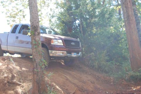 2005 Ford F-150 - A Ford F-150 truck navigates a steep dirt incline surrounded by trees.