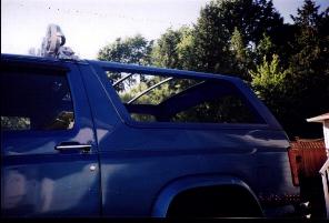 1985 Ford Bronco - Side view of a blue SUV with its removable top section exposed to the elements.