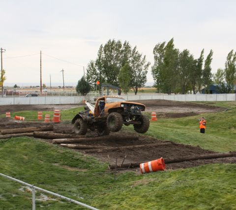 1989 Ford Bronco - A custom off-road truck soars over a log obstacle during an event.