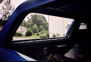 1985 Ford Bronco - Interior view from a blue SUV, looking out the rear window at a residential neighborhood. A date stamp reads 8 3 00.