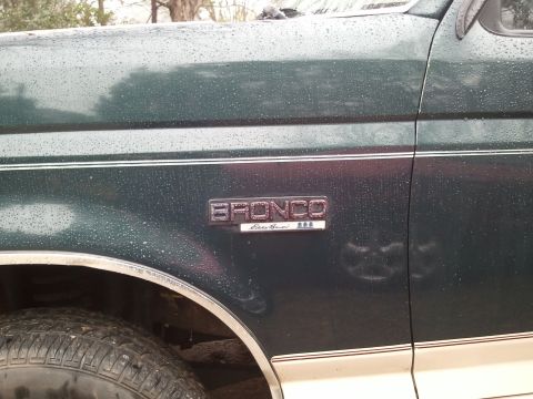 1993 Ford Bronco - A close-up of the side of a green 1993 Ford Bronco Eddie Bauer, with water droplets on the paint and a visible badge.