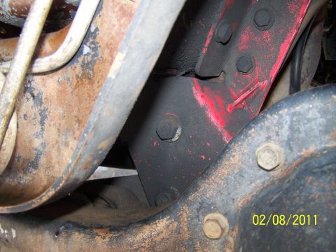 1995 Ford Bronco - Undercarriage view showing rusted metal components and a red painted bracket with bolts.