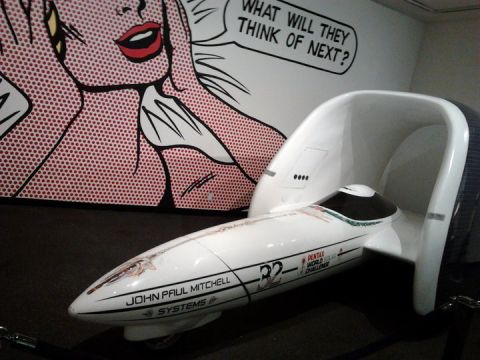 1995 Ford Taurus - A streamliner vehicle is displayed in front of a pop art mural that reads 'WHAT WILL THEY THINK OF NEXT?'.
