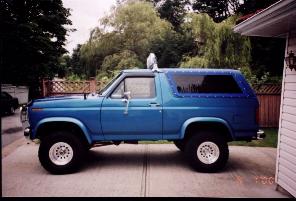 1985 Ford Bronco - This blue Ford Bronco is parked in a driveway next to a house.