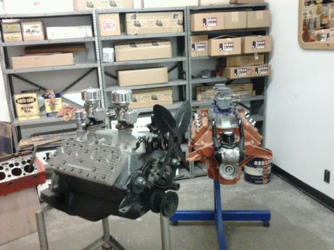 1995 Ford Taurus - Two V8 engines are displayed on stands in front of shelves stocked with boxes and cans.