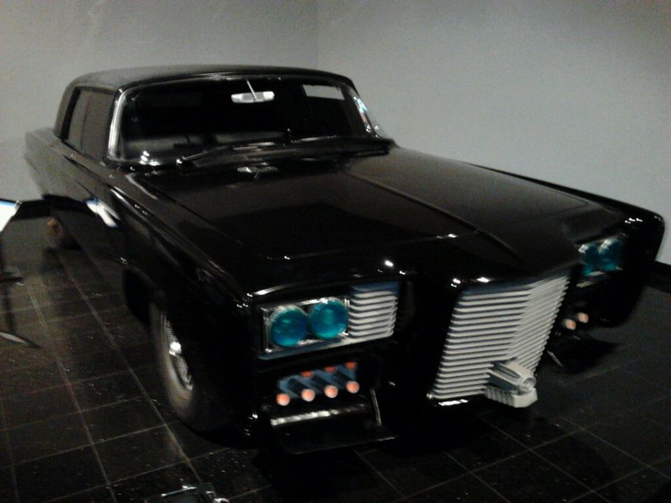 Black custom car with quad blue headlights, horizontal grille, and four small orange lights below the headlights