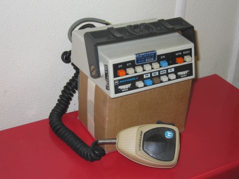 2001 Ford Crown Victoria - A Motorola radio console and its attached microphone sit on a red surface, supported by a cardboard box.